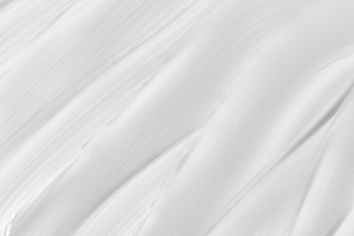 A pale white cream swatch on a neutral grey background