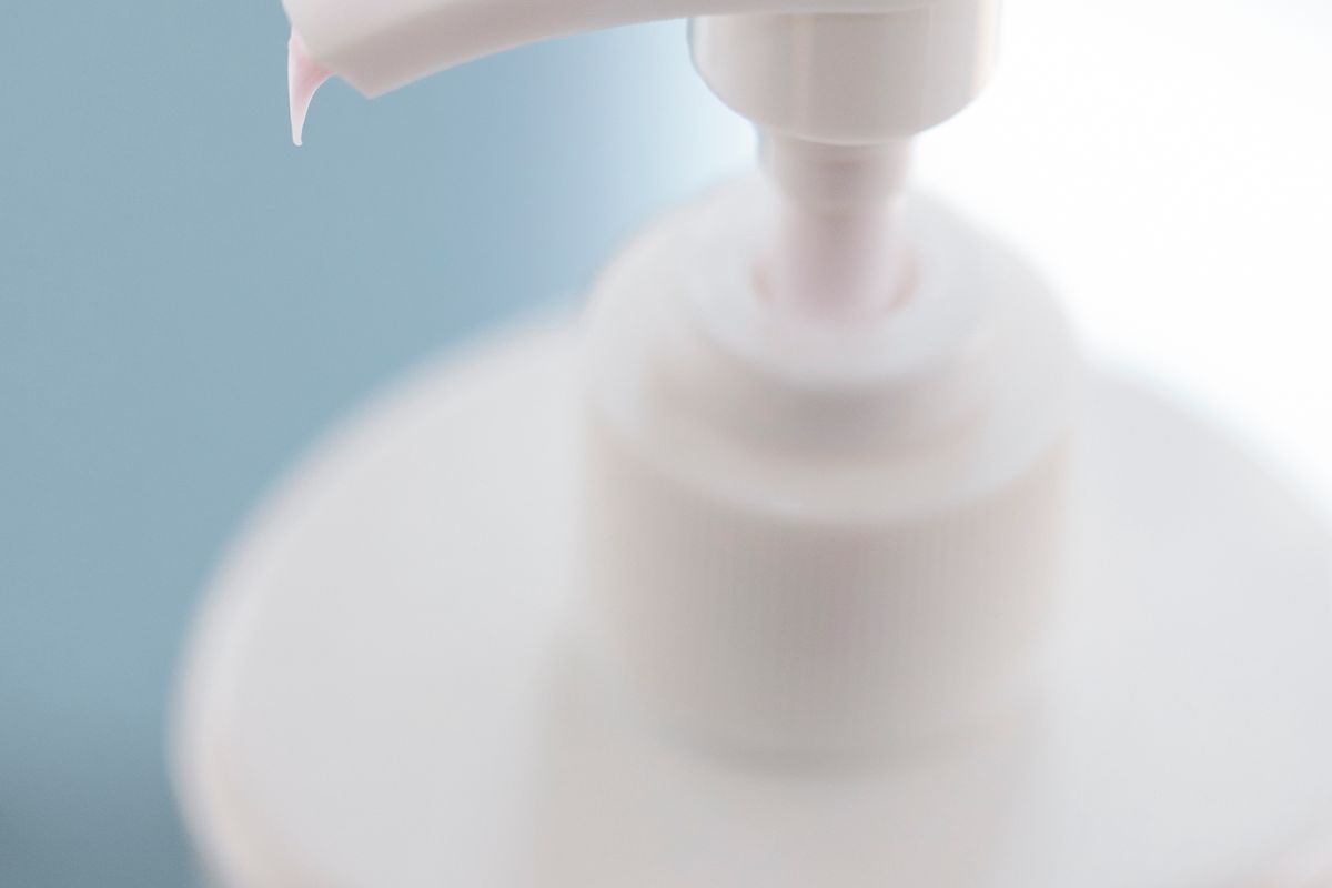 Plain white cream tube beside a folded towel on a bathroom shelf